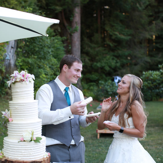 The groom holds a piece of cake, ready to feed his bride. She looks slightly hesitant.