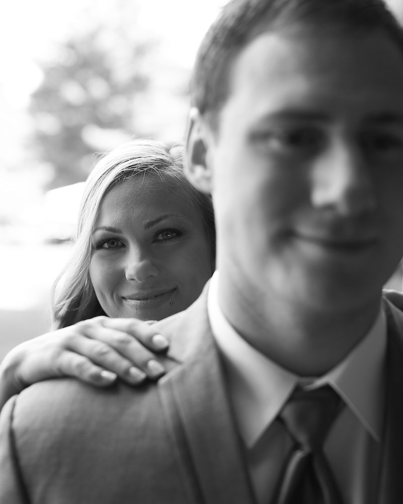 A black and white photo of the bride peeking over the groom's shoulder.