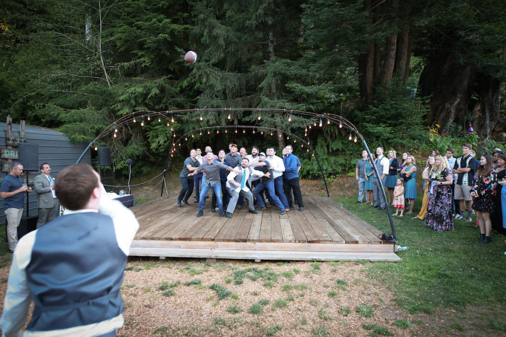 The groom, throwing a football wrapped in the garter belt, to a group of men.