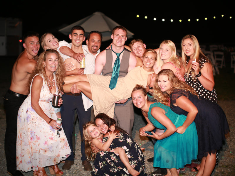 Funny group shot shows the groom holding the bride surrounded be friends and family.