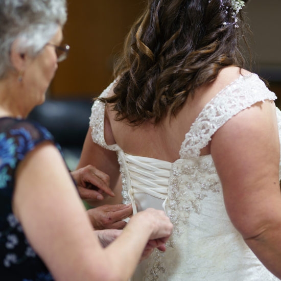 The bride stands as her mother helps tie up the back of her gown.