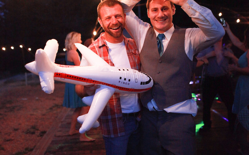 The groom posing with a friend holding a blow up airplane.