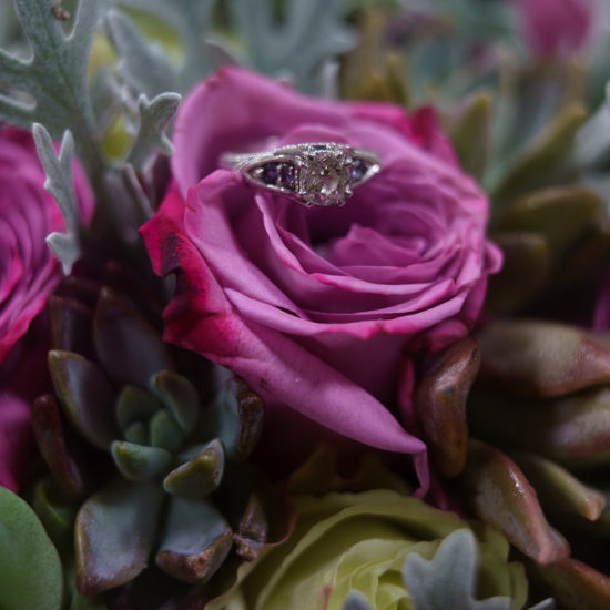 The bride's wedding ring sitting atop a pink rose in her bouquet.