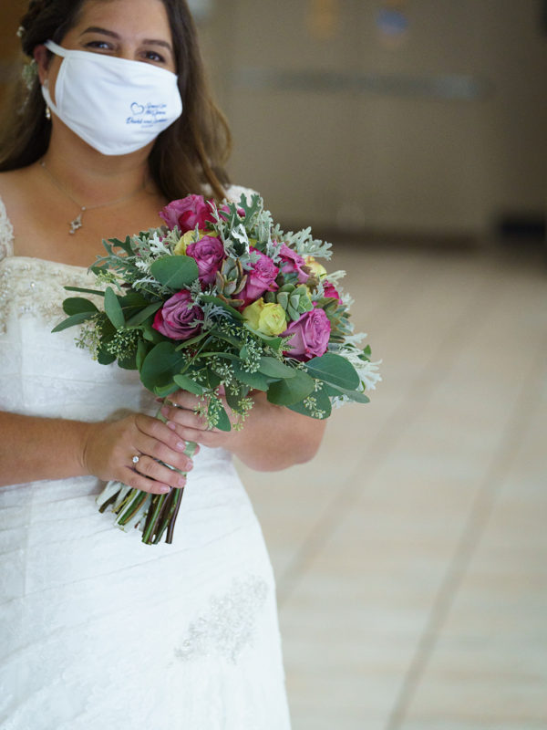 The bride holds her bouquet while wearing a white mask to prevent the spread of Covid-19.