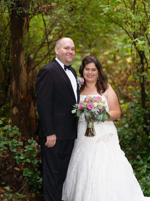 The bride and groom posing for a photo surrounded by lush green trees.