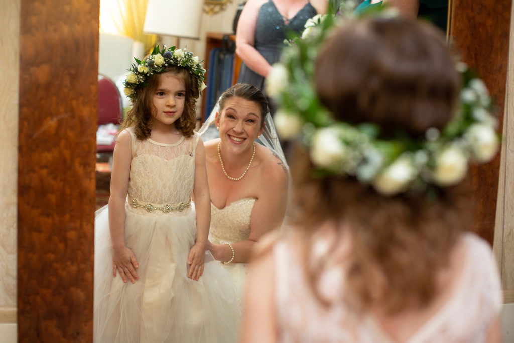 The bride squatting next to the flower girl, looking in the mirror at themselves happily.