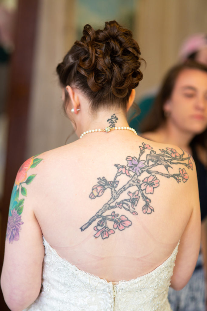 A photo of the back of the bride shows her curled hair and tattoos across her back.