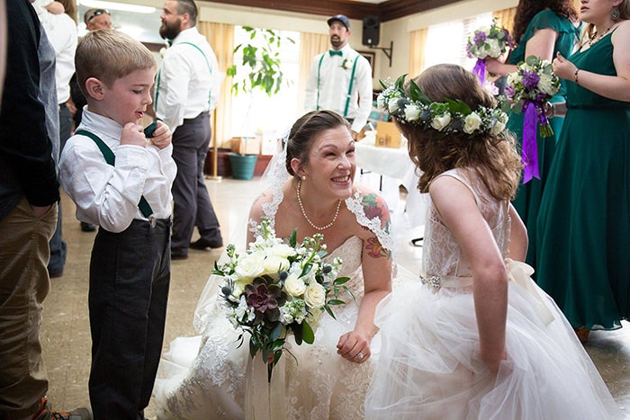 A bride crouches down to talk to the flower girl and ring bearer at the reception.